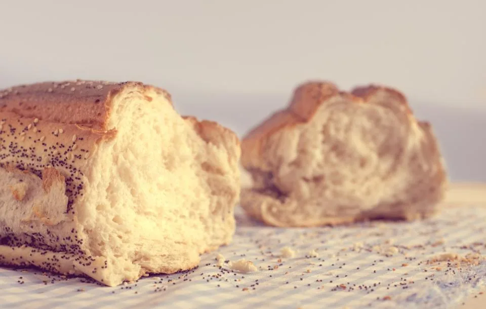 Un pain rompu en deux sur une nappe à carreaux, entouré de miettes