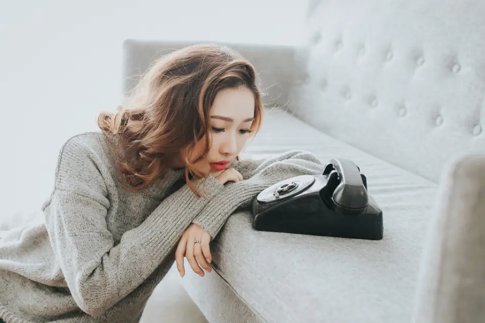 Une femme pensive attend, la tête posée près d’un vieux téléphone