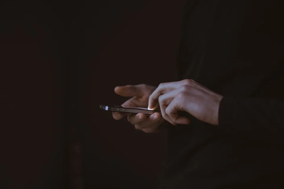 Deux mains éclairées par un écran de téléphone, en train d’écrire dans le noir