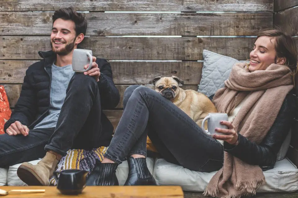 Un couple rit, assis dehors avec un carlin