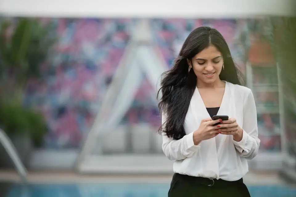 Une jeune femme sourit en écrivant sur son téléphone